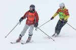 A blind skier on two skies is instructed by a volunteer.
