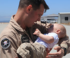 a solider in uniform holds a baby in his arms.