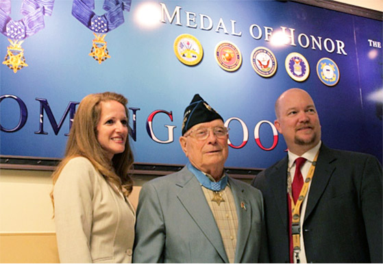 A Veteran wearing the medal of honor stands between a man and a woman A Veteran wearing the medal of honor stands between a man and a woman