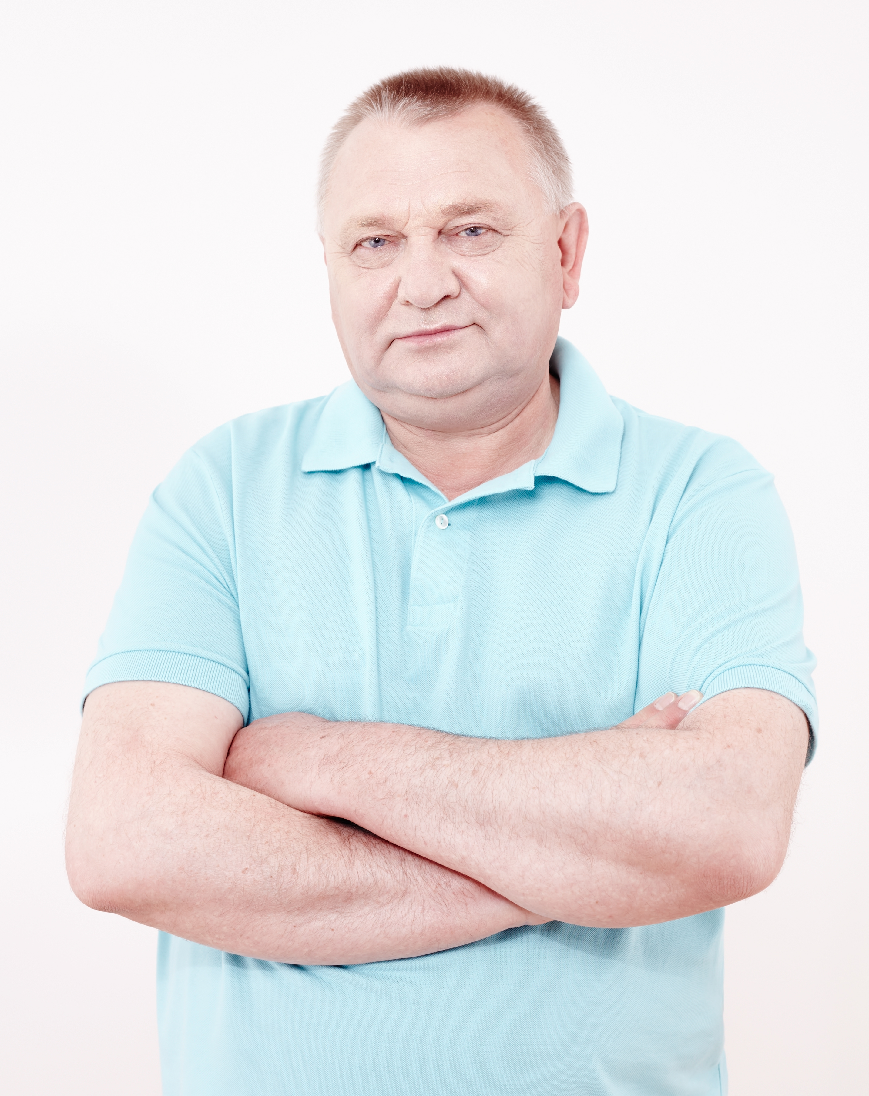 Portrait of aged man wearing blue polo shirt standing with crossed arms white wall – retirement concept